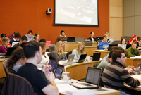 Law students sit in a full classroom, using laptop computers and books
